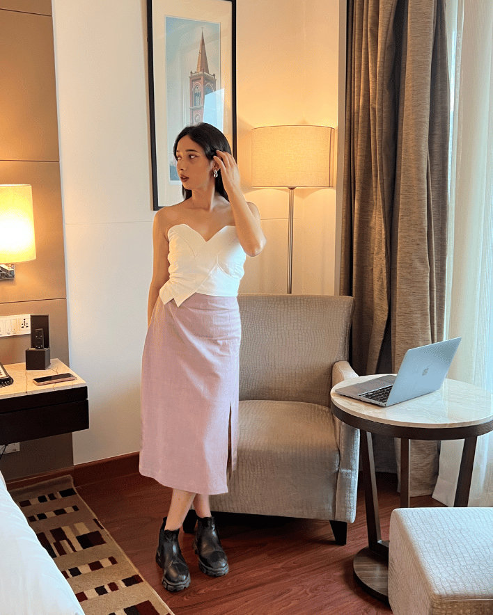 Woman in a strapless top and pink skirt standing in a hotel room.