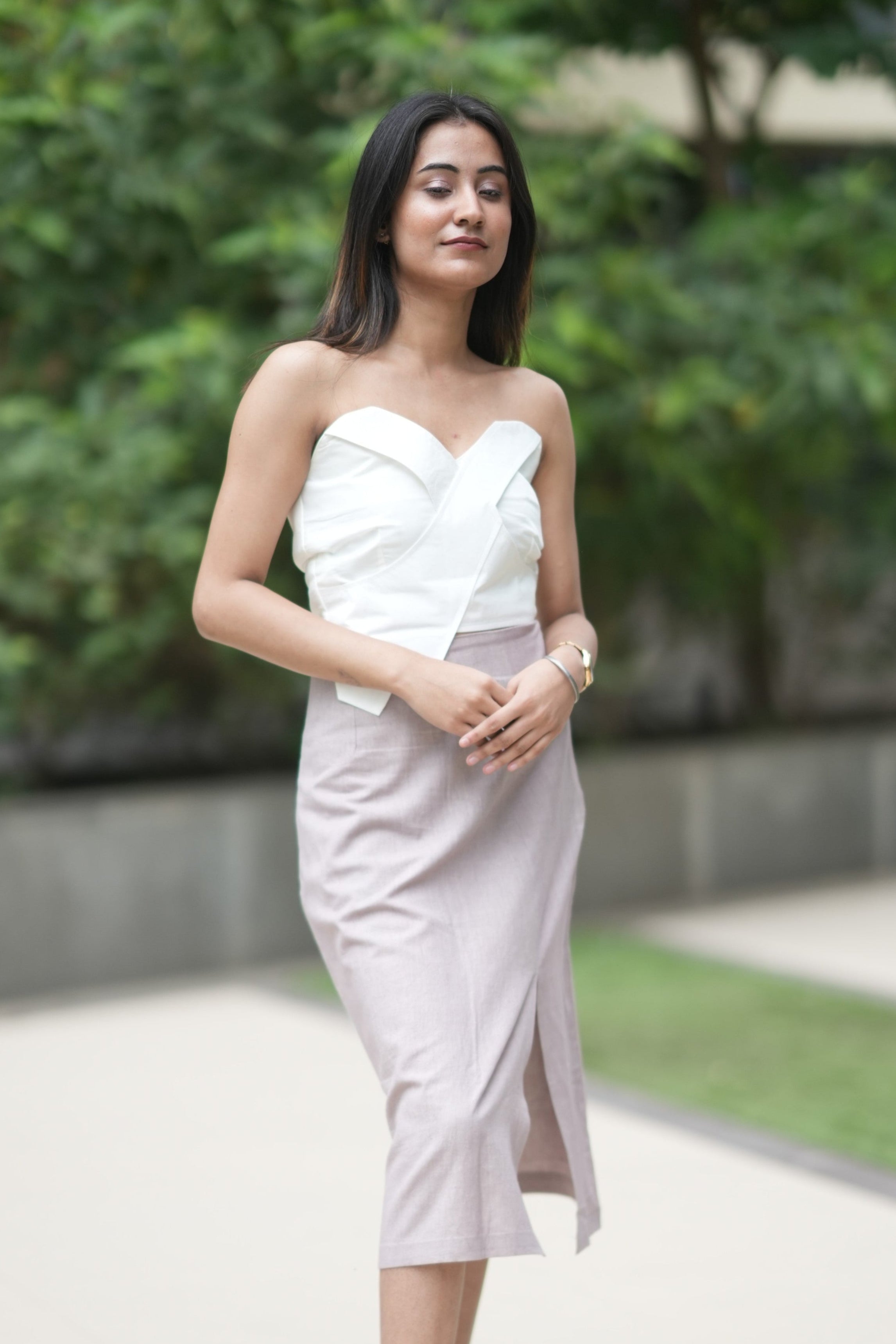 Woman in a white strapless dress standing outdoors with greenery in the background