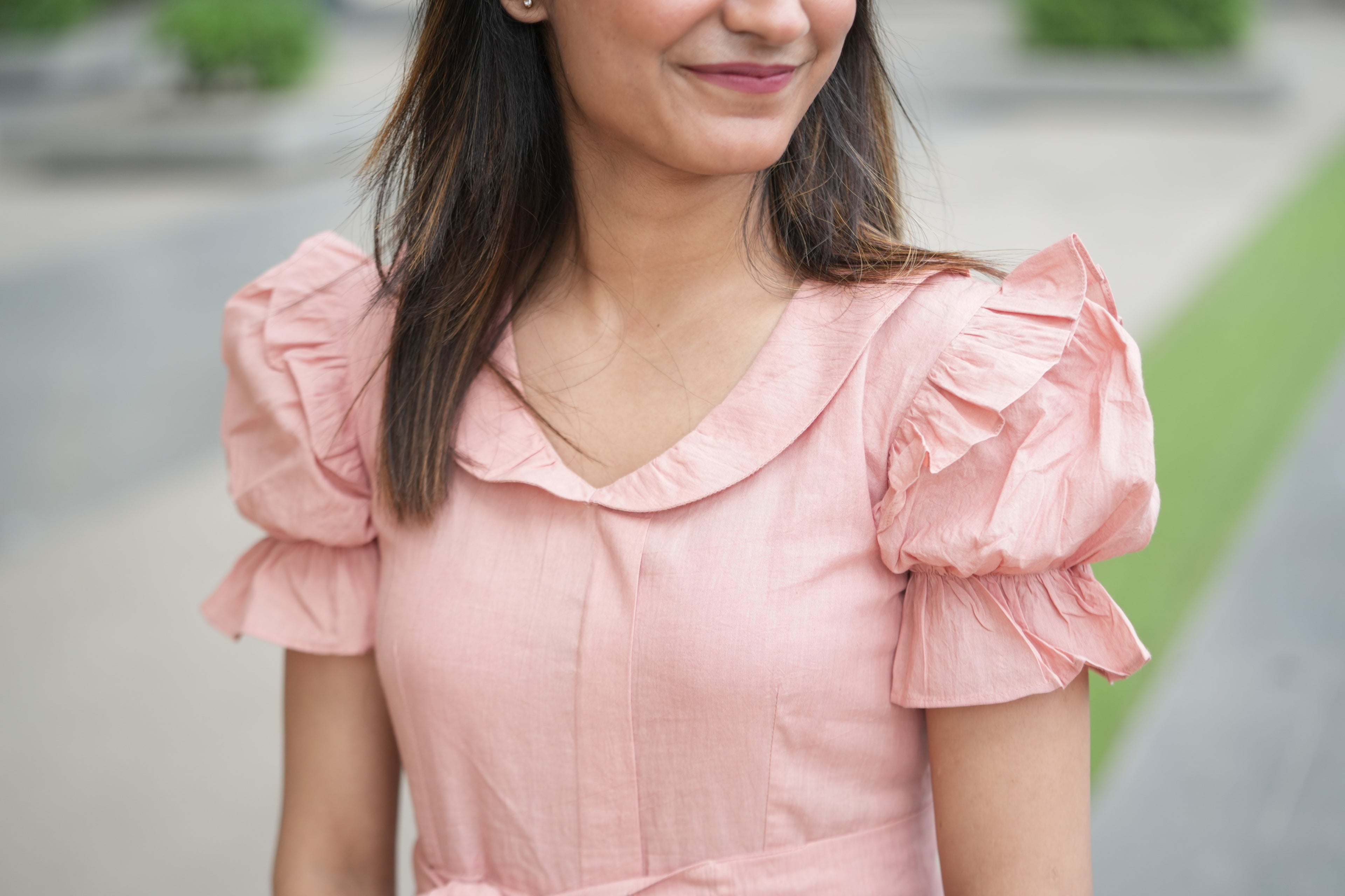 pink mini dress, peach dress, rose colored dress, Peter Pan collar dress, puff sleeve cotton dress, organic cotton clothing, sustainable vintage dress, dress with tie-belt, cottagecore aesthetic, Swaruchii fashion. A woman wearing The Rosewater Charm Dress, a short, soft-pink dress with a Peter Pan collar, puff sleeves, and a matching tie-belt, smiling in a bright, airy setting.