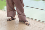 Person wearing brown pants and sandals standing on a stone floor with water in the background
