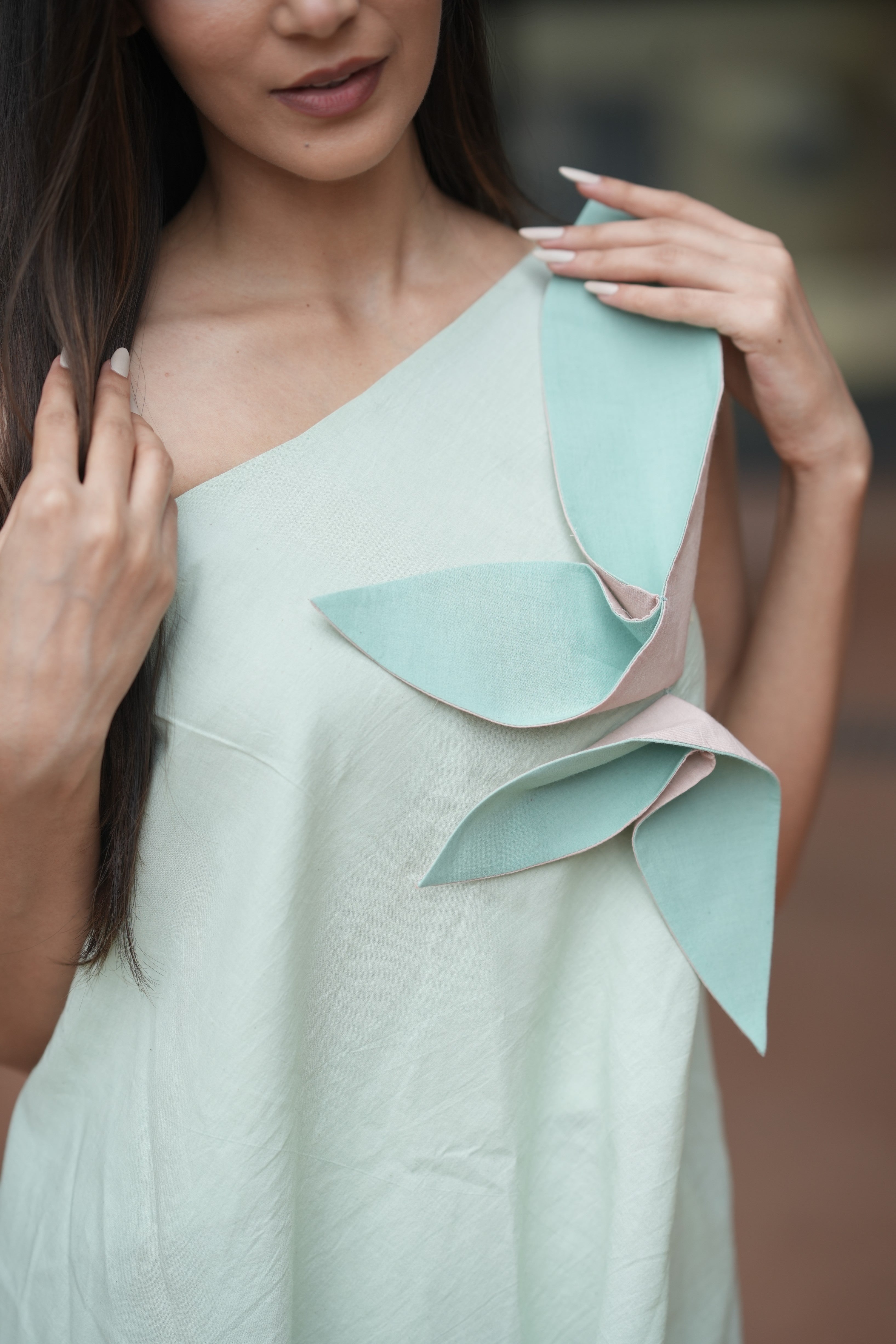 Asymmetrical light green linen dress with a large mint and white 3D leaf applique on the right shoulder, displayed on a mannequin.