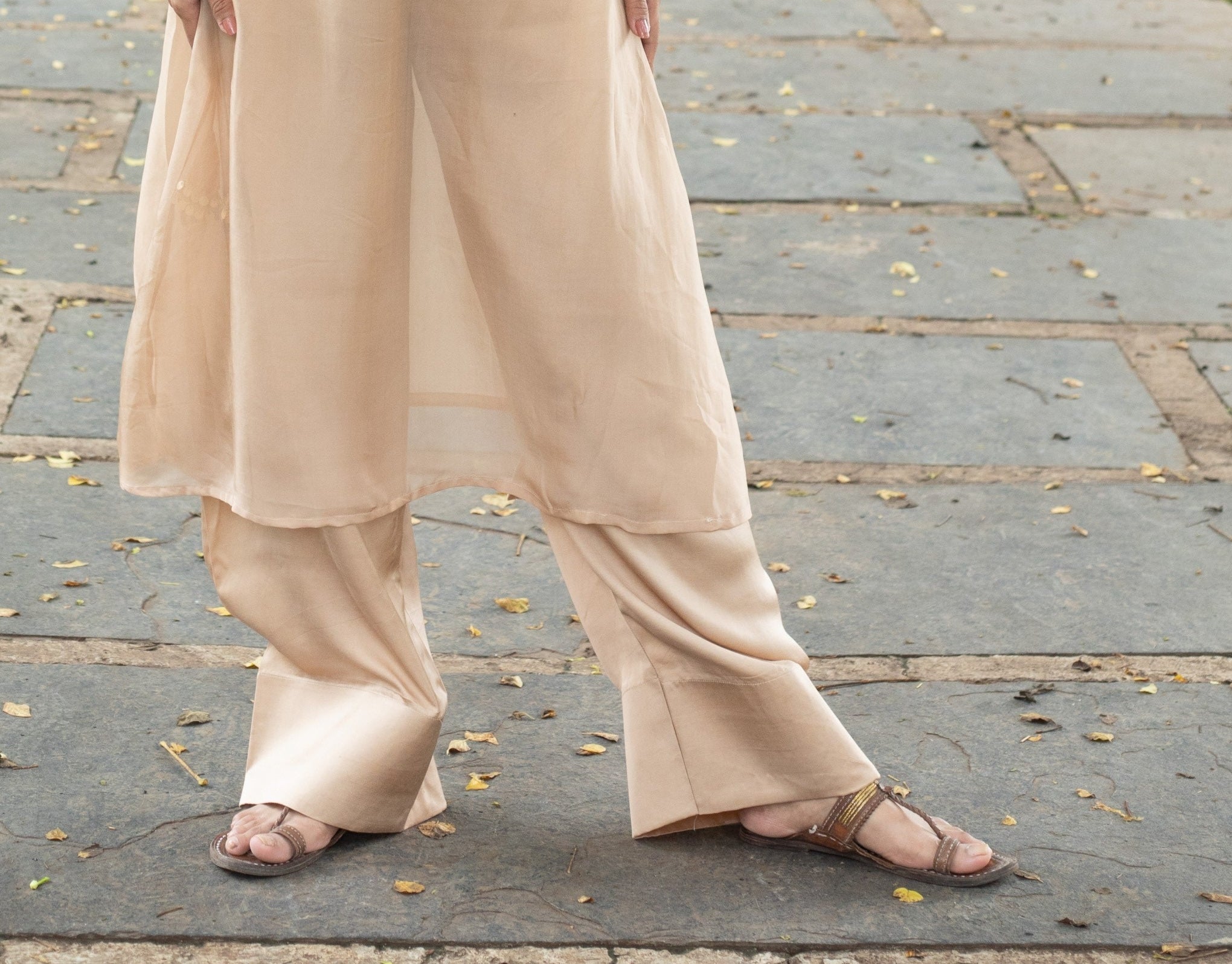 Woman in a beige outfit standing on a stone path in a park.