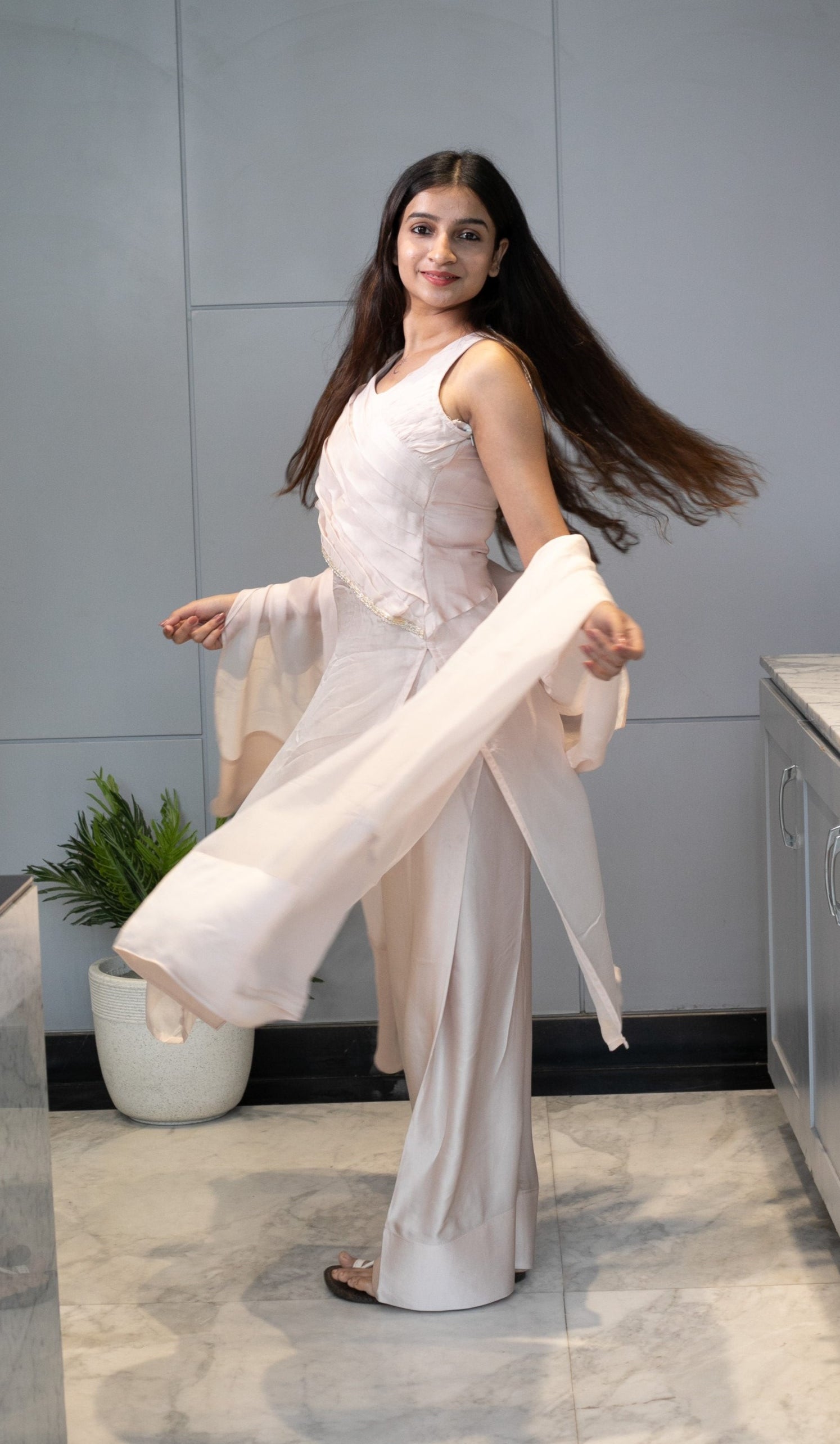 Woman in a white dress standing on a modern kitchen floor with a marble wall and stainless steel appliances.