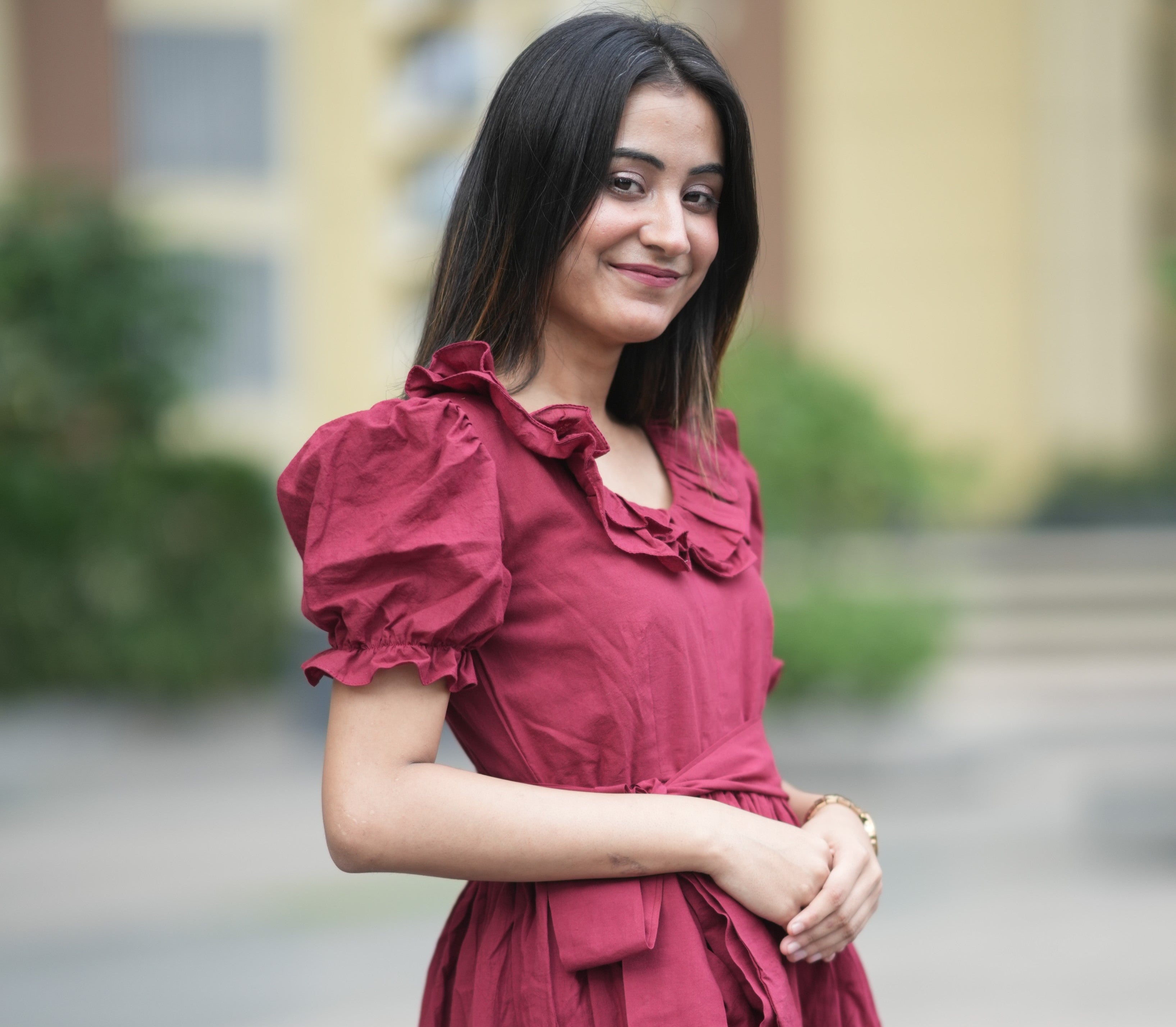 red ruffle dress, organic cotton mini dress, dress with puff sleeves, waist tie dress, fit and flare dress, vintage inspired clothing, sustainable mini dress, dress with built-in shorts and pockets, Swaruchii Veira, ruby red dress. A woman wearing The Ruby Ruffle Dress, a short ruby-red dress with puff sleeves, a ruffled neckline, and a matching fabric tie-belt, twirling outdoors with a joyful expression.