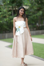 Woman in a white top and beige skirt standing outdoors with greenery in the background. 
