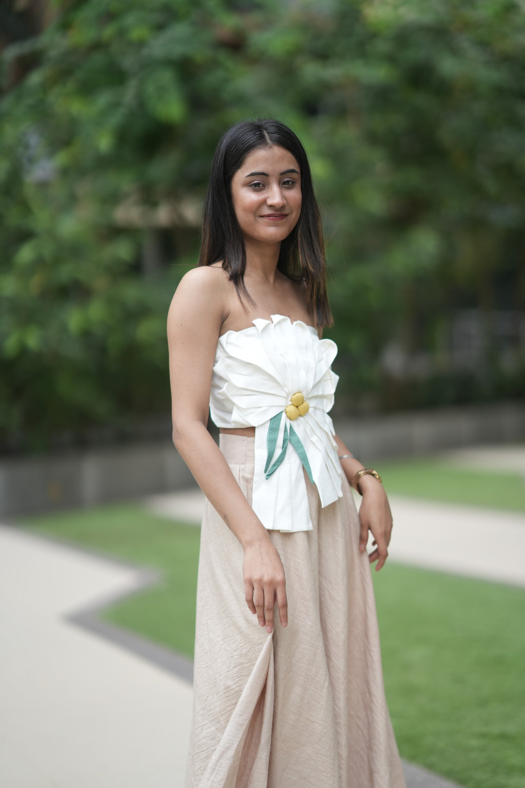 Woman wearing a floral top and beige skirt standing outdoors with greenery in the background