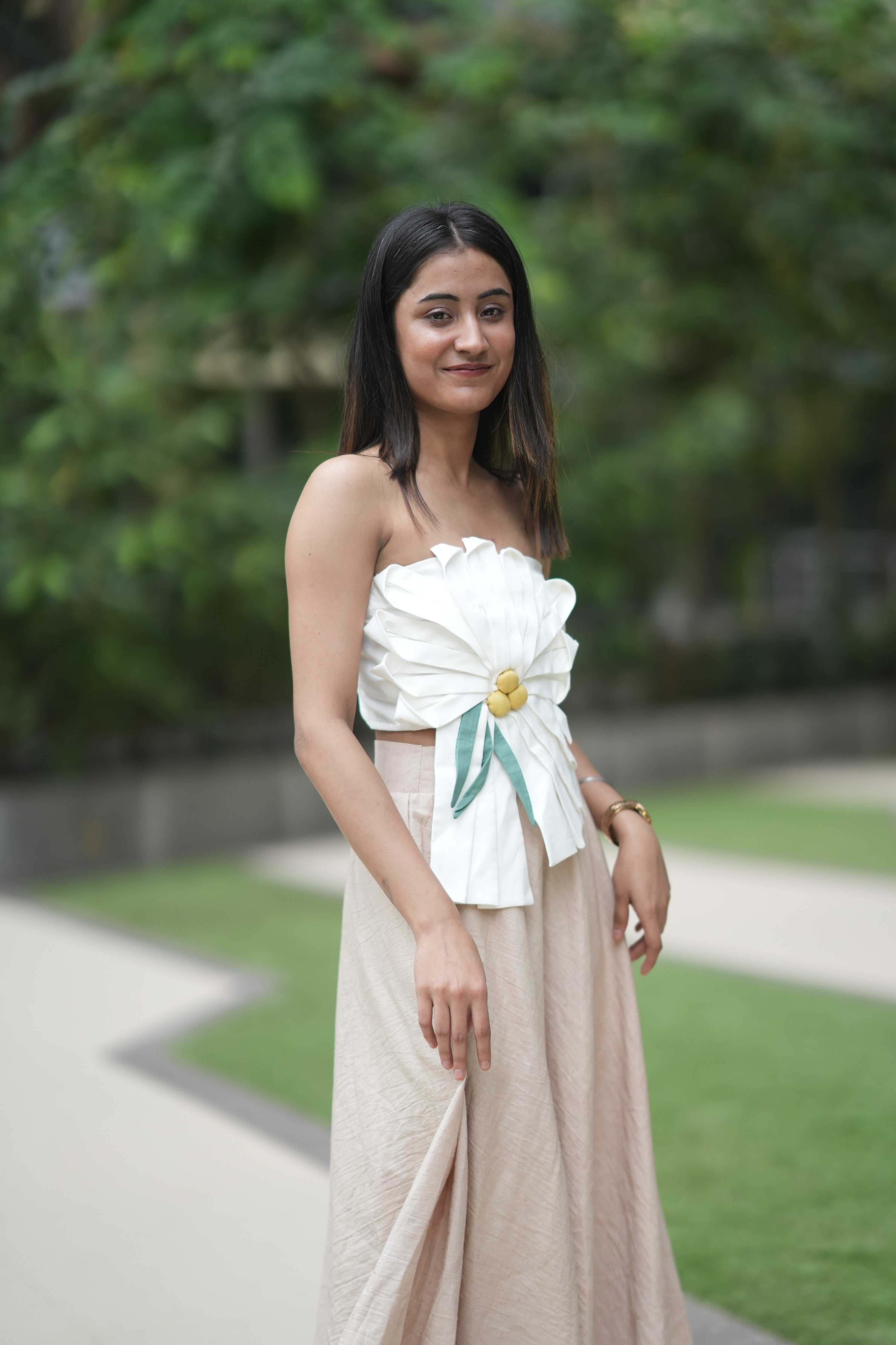 Woman wearing a floral top and beige skirt standing outdoors with greenery in the background