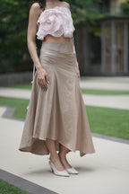Woman wearing a pink floral top and beige skirt outdoors. A woman models 'The Blush' co-ord set by Swaruchii, consisting of a pink ruffled strapless crop top and a beige asymmetrical Khadi midi skirt.